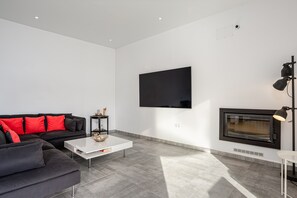A modern living room with a black sofa, white coffee table, and a flat-screen TV mounted on the wall.