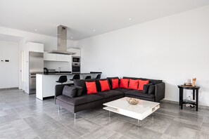 A modern living space with a kitchen, a black sectional sofa with red cushions, and a white coffee table.