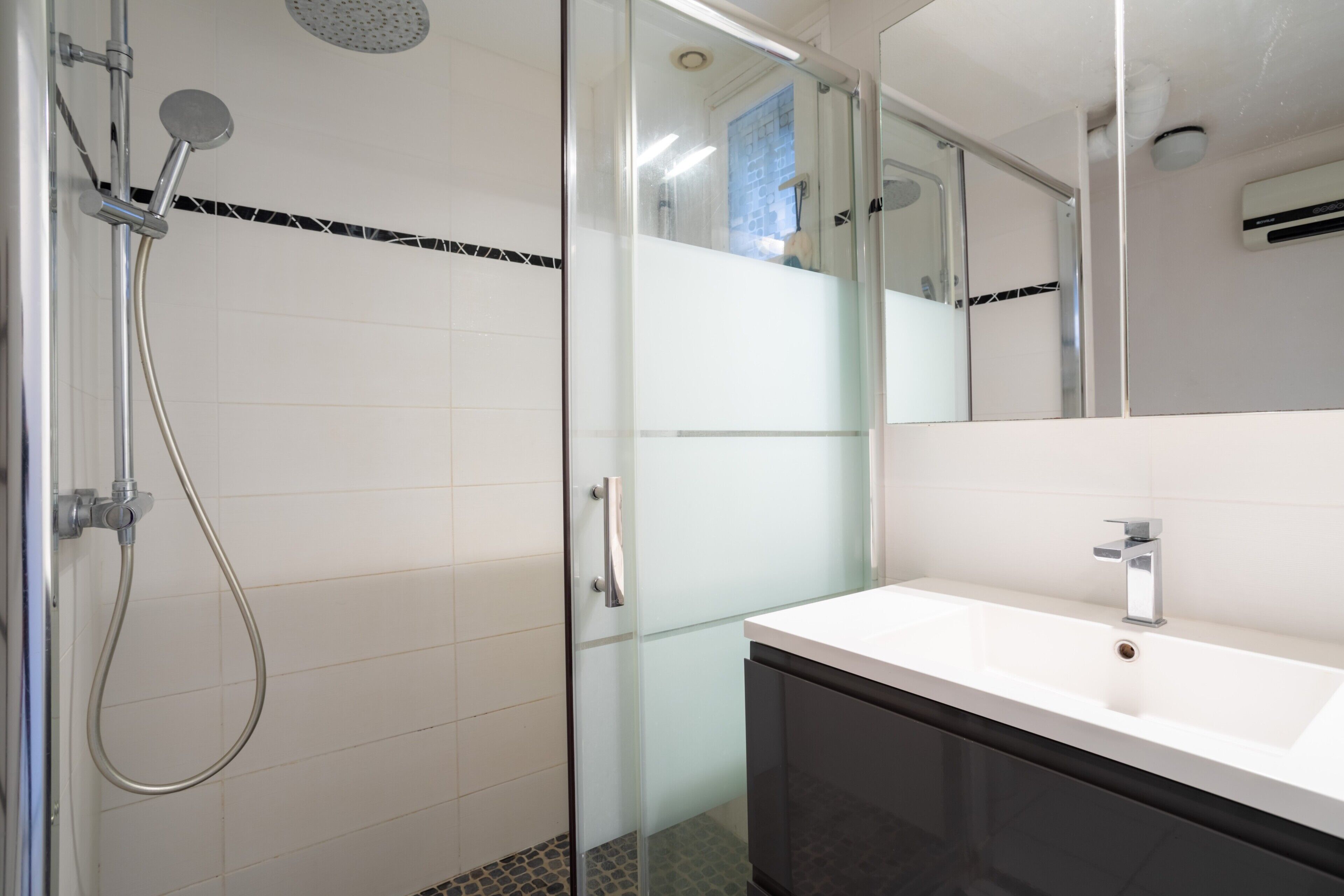 A modern bathroom with a glass shower enclosure, a white sink, and a mirror.