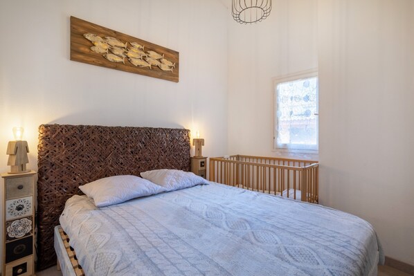 Ein Schlafzimmer mit Bett, Babybett, Wandbild und Fenster.