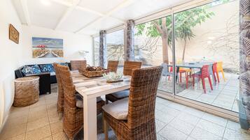 Un comedor con sillas de mimbre, una mesa de madera y un ventanal que da a una zona de estar exterior.