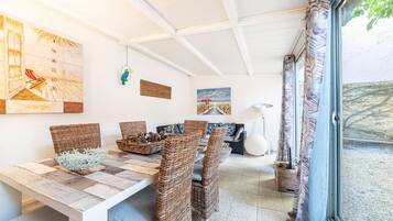 Un comedor con una mesa de madera, sillas de mimbre y un ventanal con cortinas.