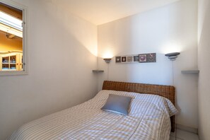 Un dormitorio con colcha a cuadros, una sola almohada, cabecero de mimbre y apliques de pared.