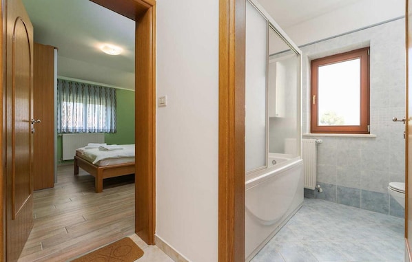 Habitación de hotel con armario de madera, cama con edredón blanco, baño con bañera y ventana con marco de madera.