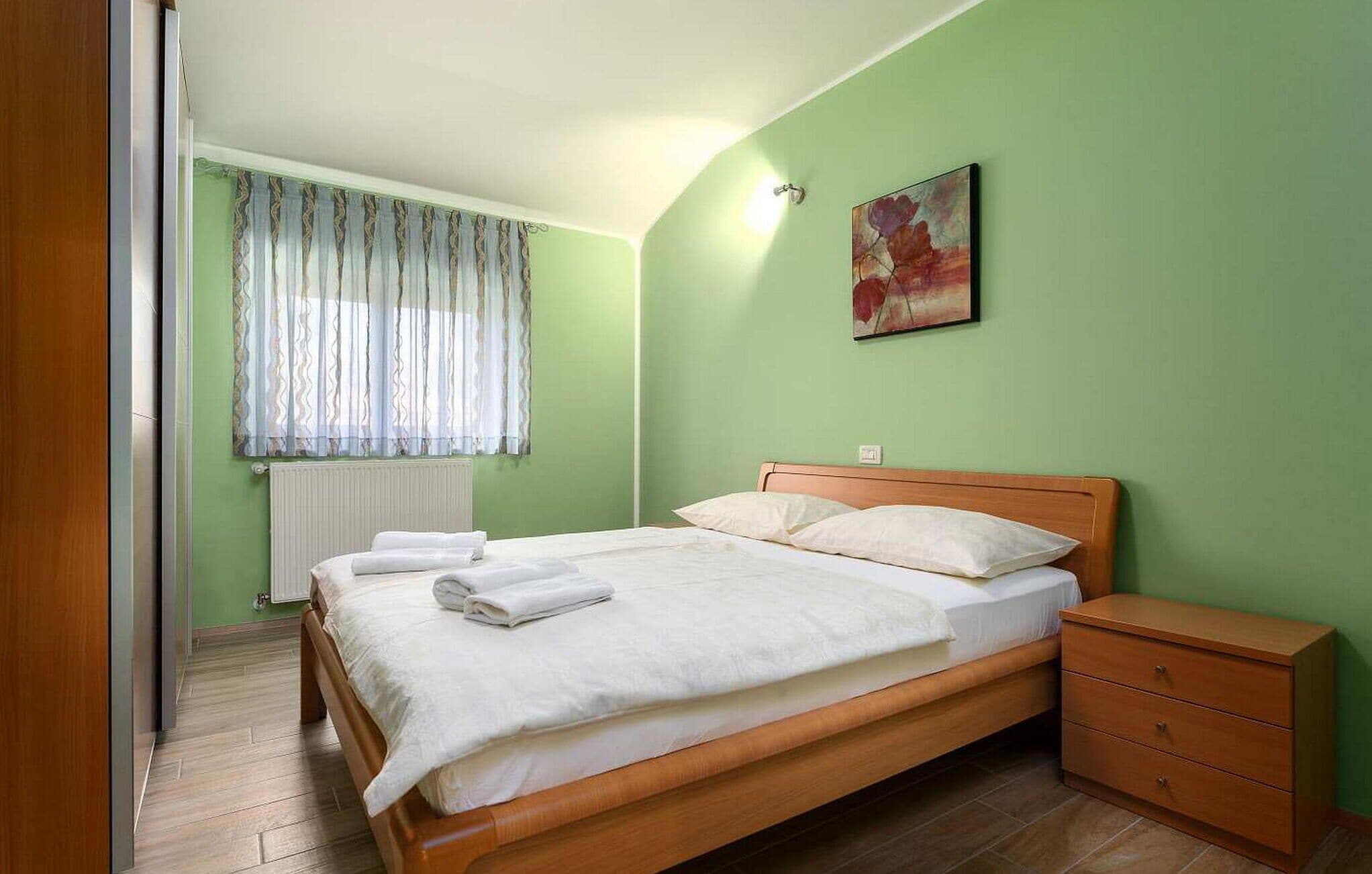 A bedroom with a wooden bed, a nightstand, a radiator, and a window with curtains.