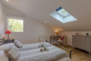 Une chambre avec un puits de lumière, un lit avec des oreillers, un bureau, une chaise, une commode et une lampe.