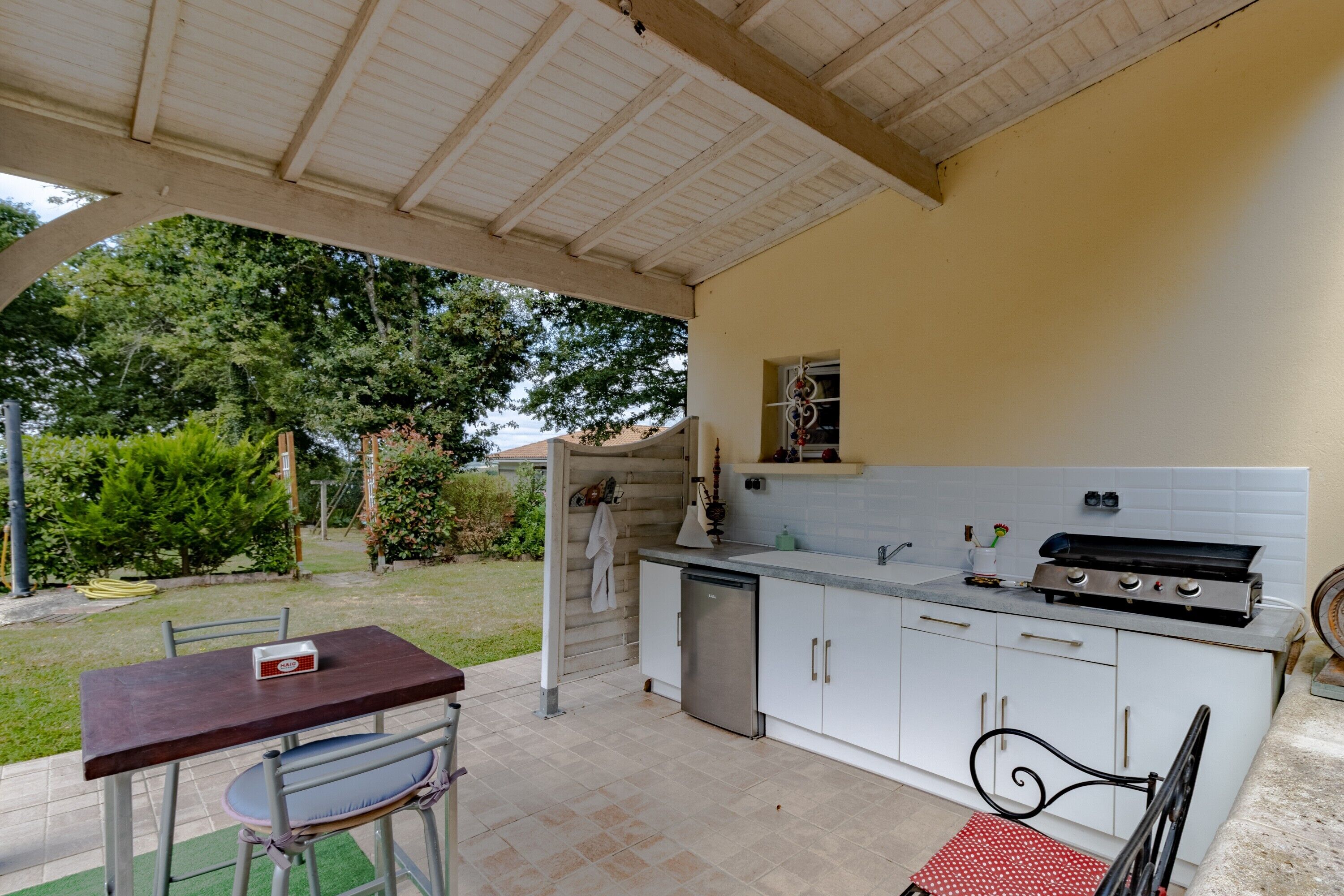 A covered outdoor kitchen with a dining area, a grill, and a sink.