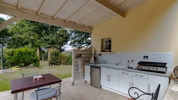 A covered outdoor kitchen with a dining area, a grill, and a sink.
