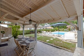 Une terrasse couverte avec une piscine, des sièges d’extérieur et une vue sur le jardin arrière.