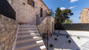 Ein Steinhaus mit einer Treppe, die zu einem Balkon führt, umgeben von Kies und kleinen Pflanzen.