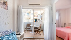 A room with a bed, a sofa, a dining table with chairs, a sliding glass door leading to a balcony, and a small table with a lamp. - Apartment 'Córdula' with Wi-Fi and Air Conditioning (Es Pujols)