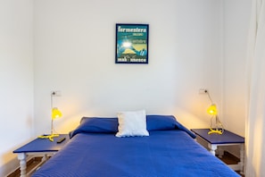 A bedroom with a bed, two bedside tables, a nightstand, a pillow, and a wall-mounted poster.