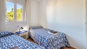 A room with two beds, a desk, a lamp, and a window with curtains. - Apartment 'Isla Blanca' with Air Conditioning (Es Pujols)
