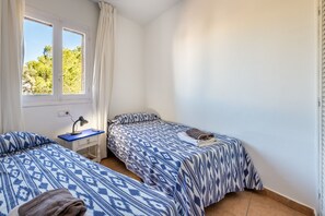 Une chambre avec deux lits, un bureau, une lampe et une fenêtre avec des rideaux.