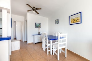 A dining area with white chairs and a blue table, a ceiling fan, and framed artwork on the walls.