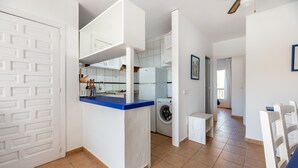 A compact kitchen with a washing machine, a dining area with chairs, and a white door. - Apartment 'Isla Blanca' with Air Conditioning (Es Pujols)