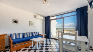 A room with a checkered floor, a sofa with striped cushions, a white table, and a balcony with a view. - Apartment 'Apartamento Bilo 303' with Lake View, Wi-Fi and Air Conditioning (Es Pujols)