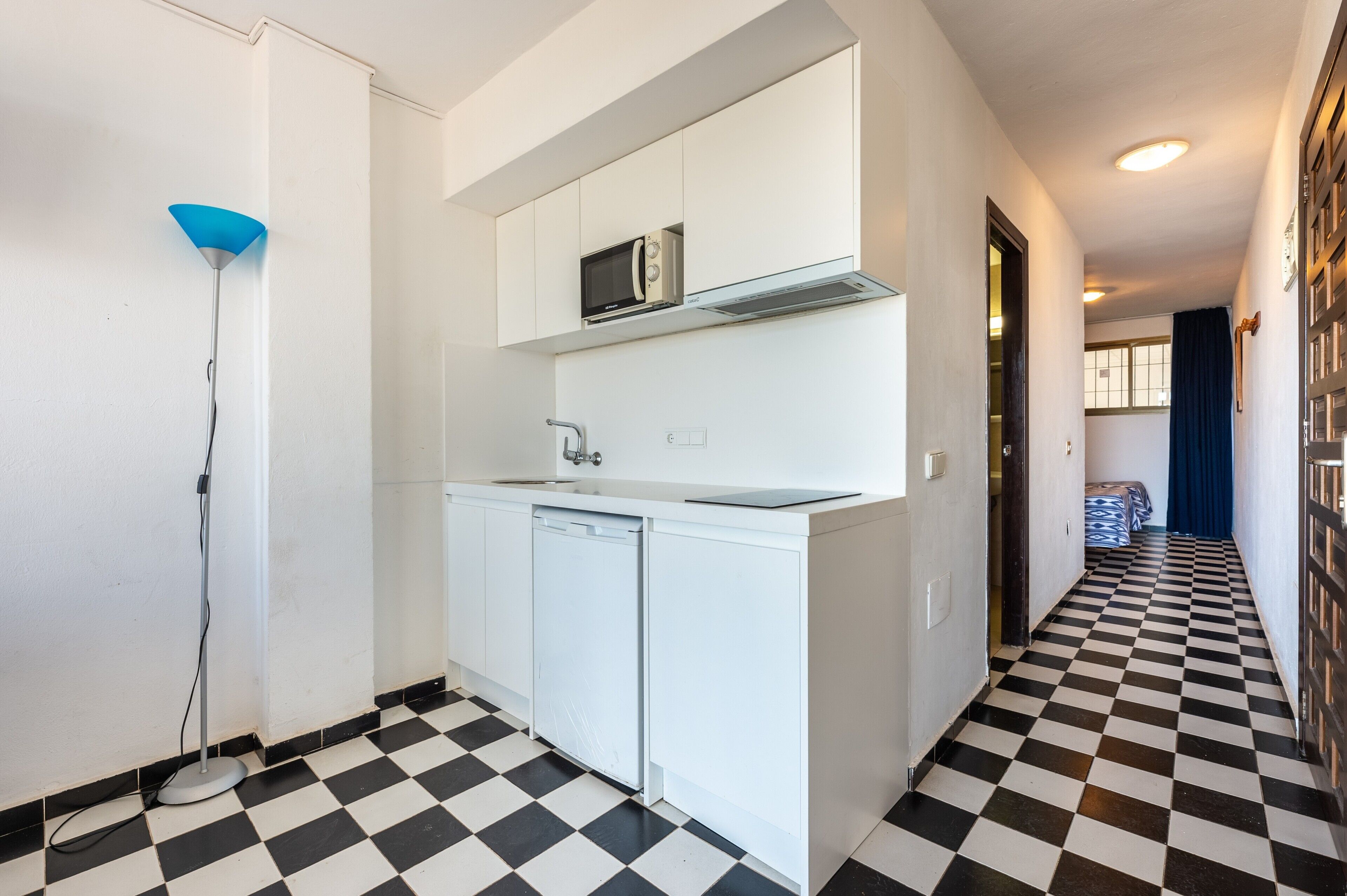 A compact kitchen with a microwave, dishwasher, and a blue floor lamp.