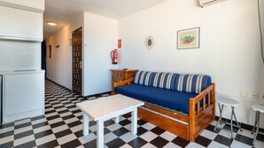 A compact living space with a kitchenette, a sofa, a small table, and a fire extinguisher mounted on the wall. - Apartment 'Apartamento Bilo 303' with Lake View, Wi-Fi and Air Conditioning (Es Pujols)
