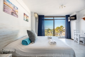 Une chambre d’hôtel avec un lit, un bureau, une télévision et un balcon offrant une vue.