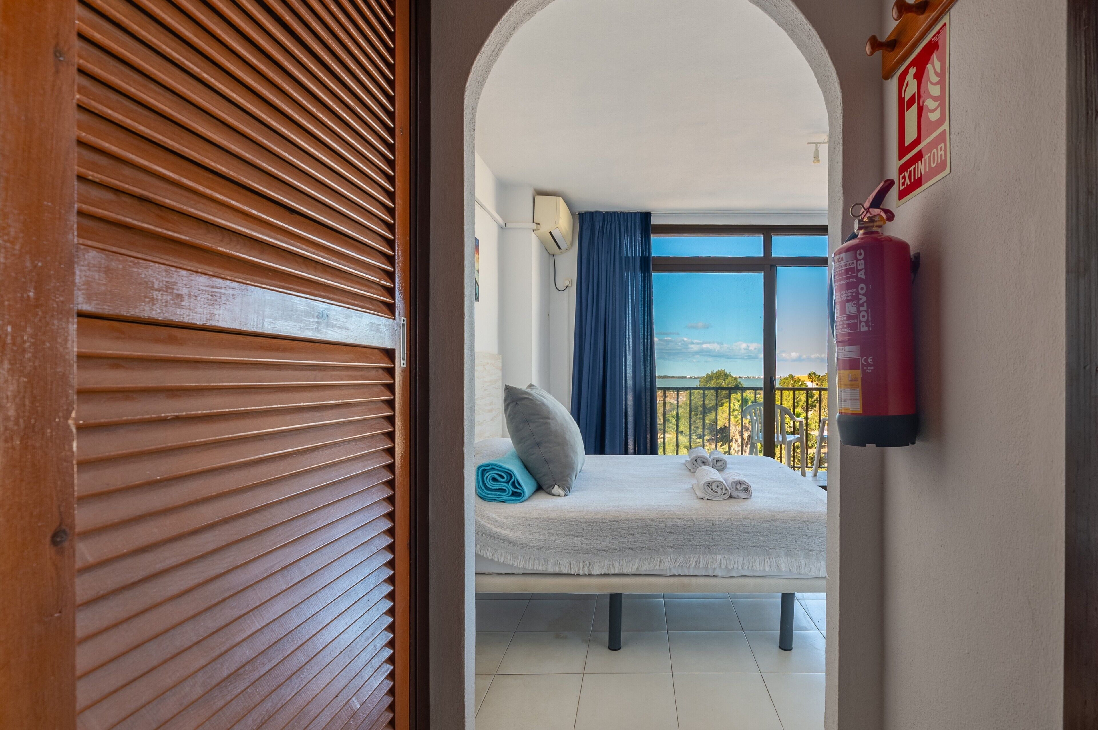 Una habitación con cama, ventana con vistas, extintor y puerta.