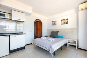 Une chambre à coucher avec un lit, une table de chevet, une petite armoire blanche, un four à micro-ondes et une porte en bois.