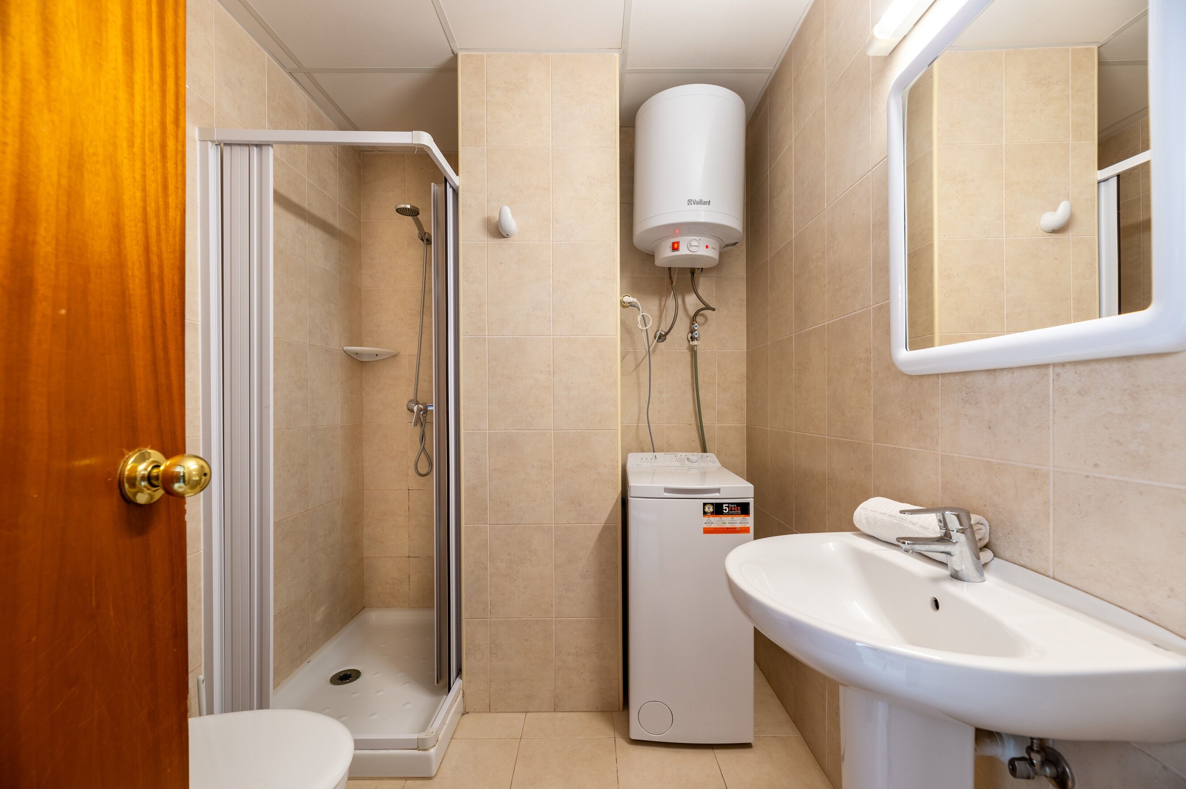 A bathroom with a shower, toilet, and sink, equipped with a water heater and a small heater unit.