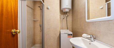 A bathroom with a shower, toilet, and sink, equipped with a water heater and a small heater unit.
