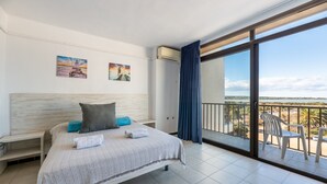 Habitación de hotel con cama, balcón con sillas y obras de arte en las paredes.
