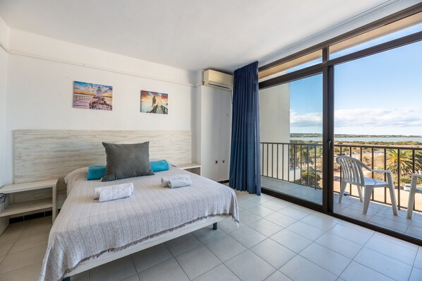 A hotel room with a bed, a balcony with chairs, and artwork on the walls.