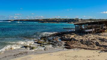 A coastal beach with rocky terrain, a wooden pier, and a small building.