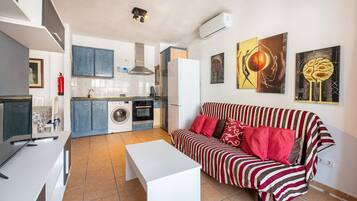 Un espacio habitable compacto con kitchenette, un sofá, una mesa blanca y obras de arte en las paredes.