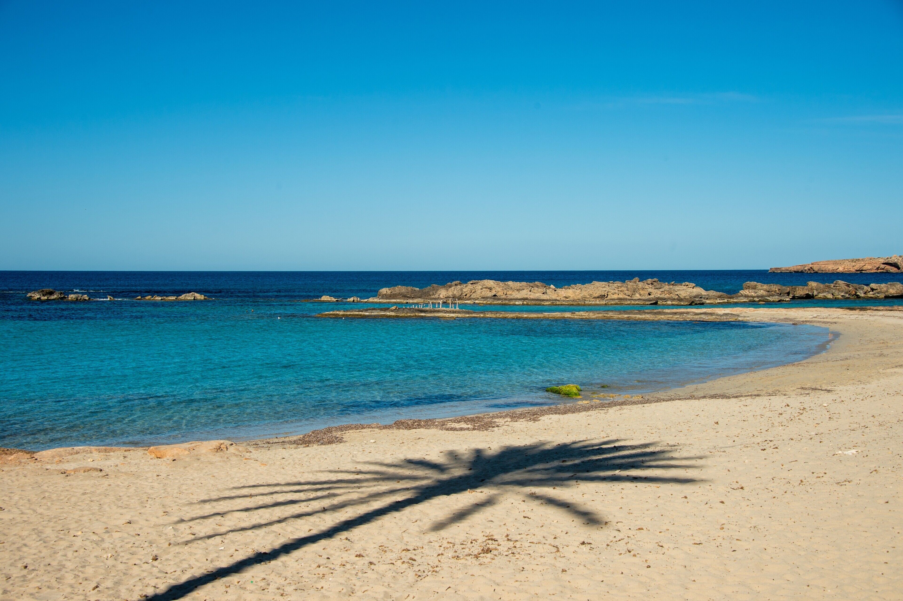 A beach with clear blue water, sandy shore, and rocky outcrops.