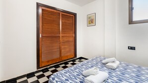 A bedroom with a checkered floor, a bed with a patterned bedspread, a wooden closet, and a small window. - Holiday Apartment "Bilo 301" with Private Terrace & Wi-Fi (Es Pujols)