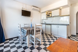 A kitchen with a checkered floor, a dining table with chairs, a TV mounted on the wall, and white cabinets.