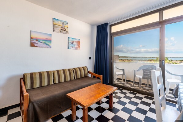 A room with a checkered floor, a sofa, a table, and a balcony with chairs. - Holiday Apartment "Bilo 301" with Private Terrace & Wi-Fi (Es Pujols)