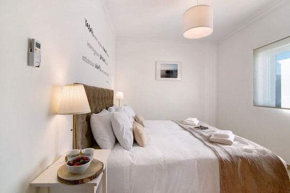 Une chambre d’hôtel bien rangée, avec un lit, une table de chevet, une lampe, des œuvres d’art accrochées au mur et une fenêtre.