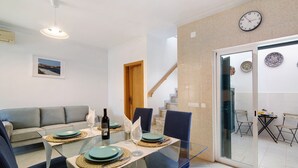 A dining area with a glass table, blue chairs, and a sofa.