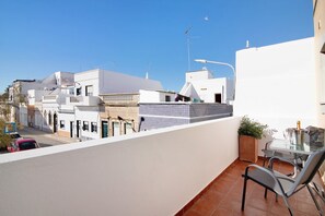 Un balcon avec une table et des chaises, un pot de fleurs et une vue sur les bâtiments voisins.