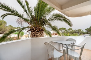 A balcony with a palm tree, white chairs, and a table. - Apartment 'Apartamento Trilo 12' with Wi-Fi (Es Pujols)