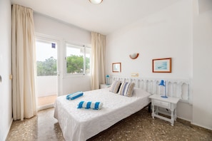 A bedroom with a bed, a nightstand, a lamp, and a view of the outdoors. - Apartment 'Apartamento Trilo 12' with Wi-Fi (Es Pujols)