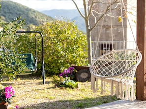 Un fauteuil suspendu, une chaise verte et une plante en pot dans un jardin, avec une chaîne de montagnes en arrière-plan.