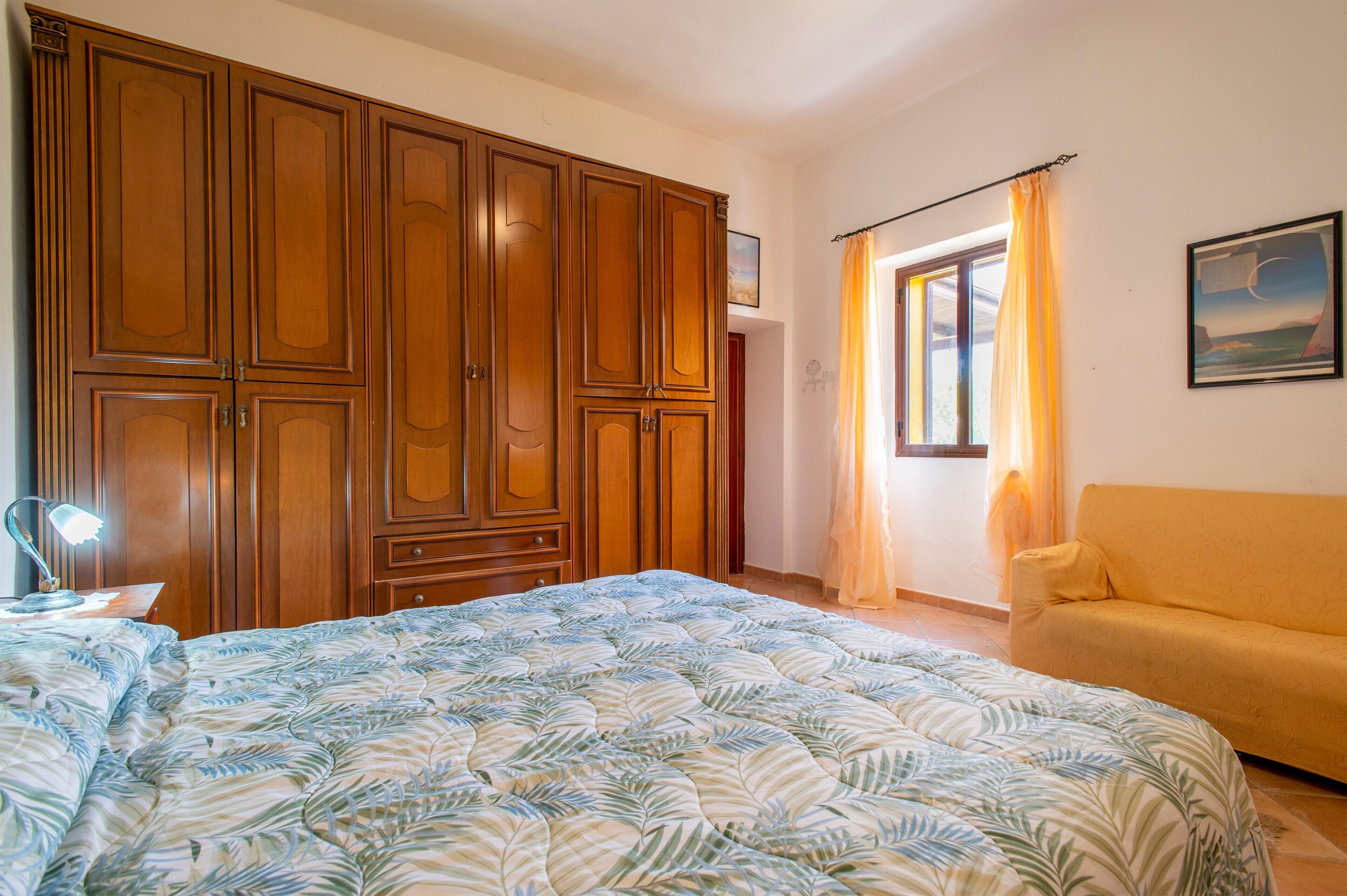 Een slaapkamer met een groot bed, een houten garderobe, een gele bank en een raam met gordijnen.