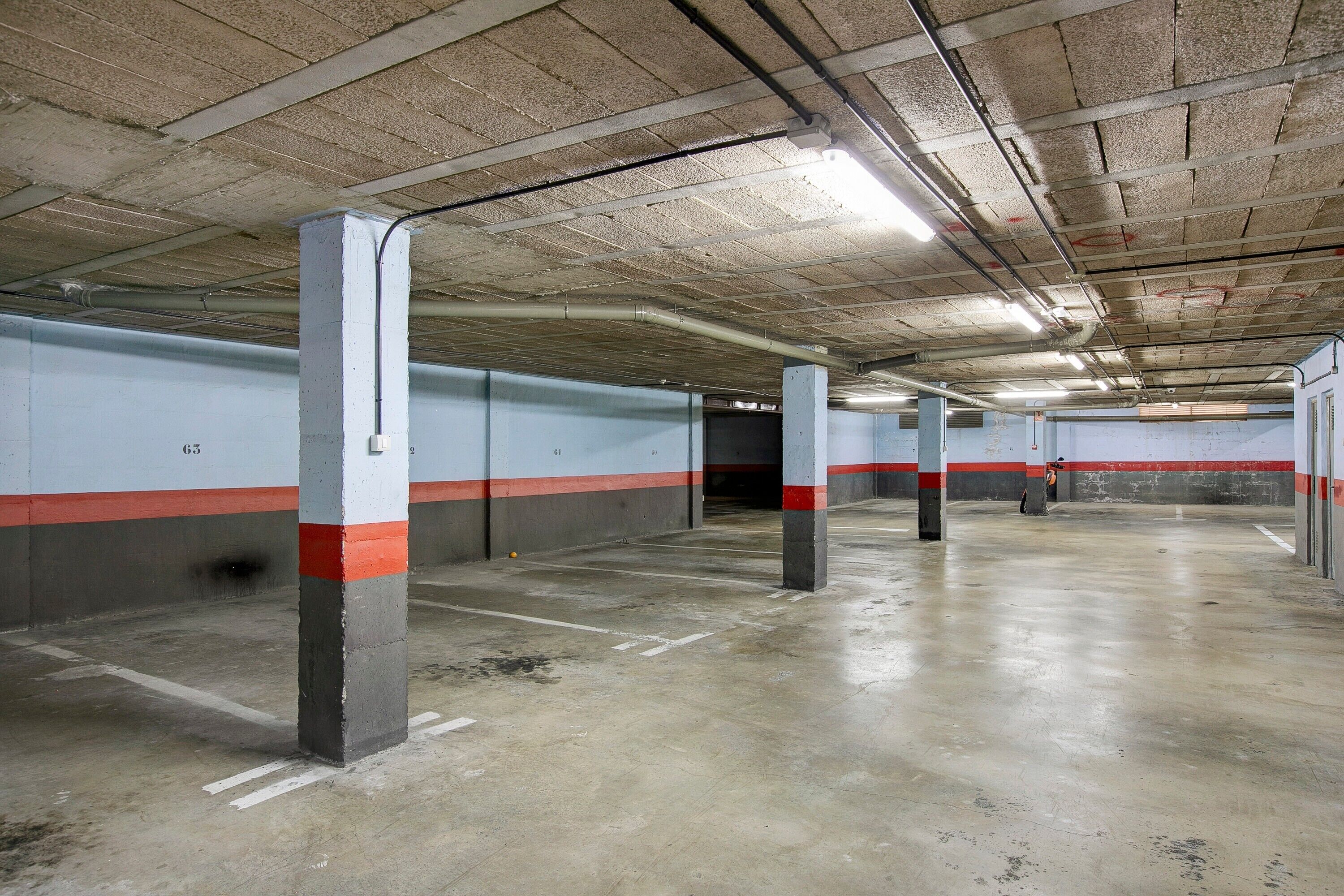 Eine überdachte Parkgarage mit Betonpfeilern, weißen und roten Streifen an den Wänden und einem sauberen, leeren Boden.