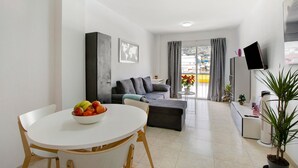 Ein modernes Wohnzimmer mit Esstisch, einer Couch, einem Fernseher und einer Topfpflanze.
