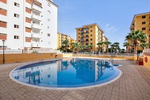 Une piscine dotée d’une terrasse carrelée, entourée d’immeubles à plusieurs étages avec des balcons.