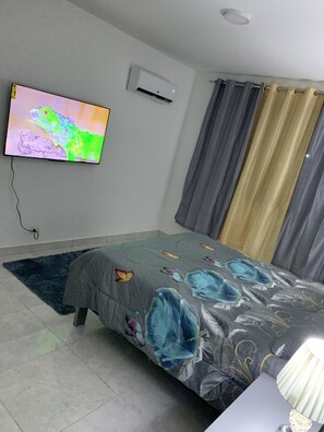 A bedroom with a bed, a TV mounted on the wall, an air conditioner, and curtains.