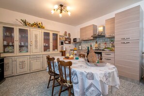 Un coin repas avec une table dressée pour quatre personnes, entourée de chaises en bois. Un lustre est suspendu au plafond, et il y a des armoires avec des portes en verre sur le côté gauche.