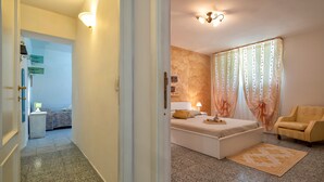 Une chambre d’hôtel avec un lit, une chaise, une table de chevet, une lampe et une fenêtre avec des rideaux.