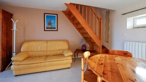 Un salón con un sofá amarillo, una escalera de madera y un cuadro en la pared.